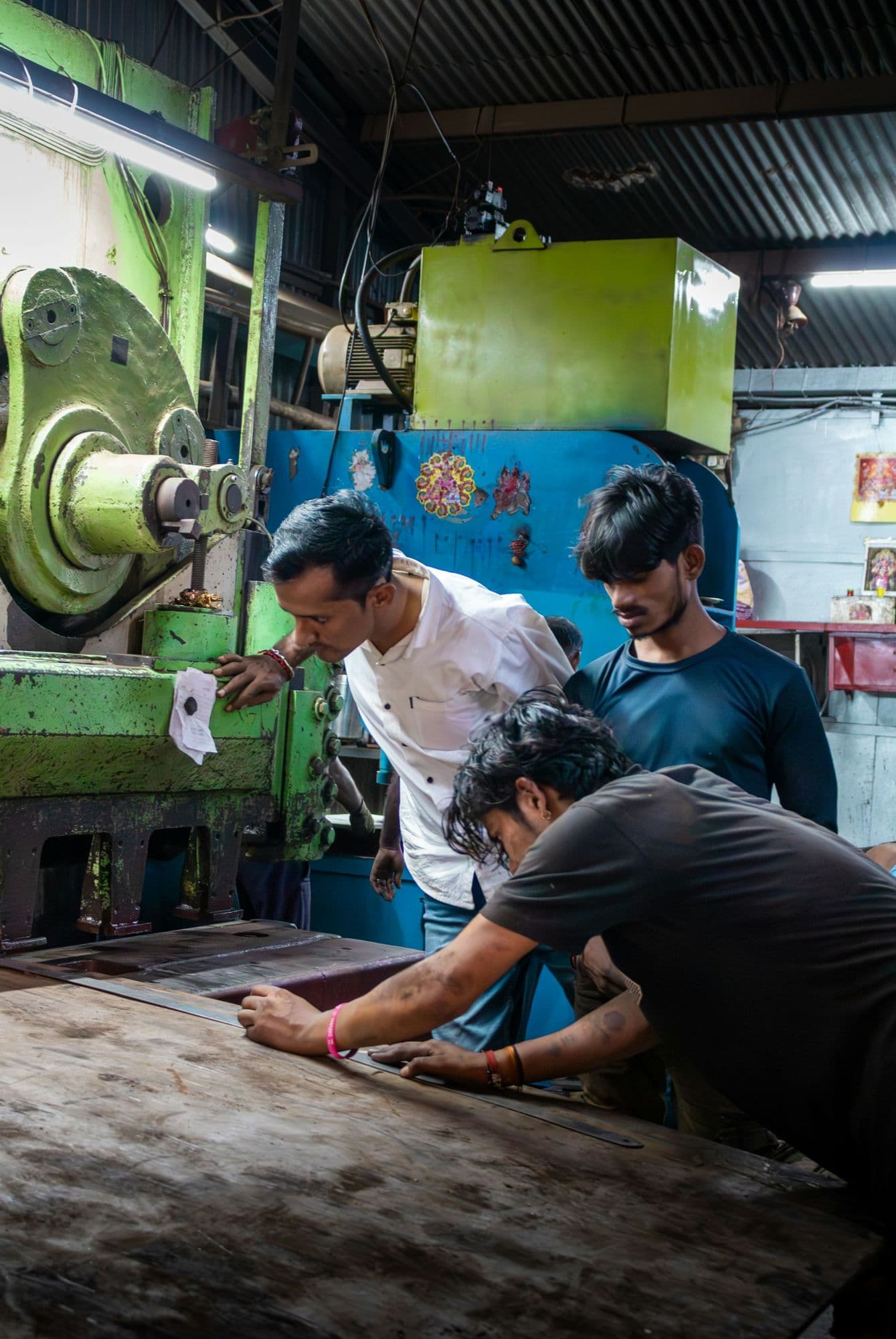 Supervisor and workers positioning a steel sheet under a shearing press in a machine shop