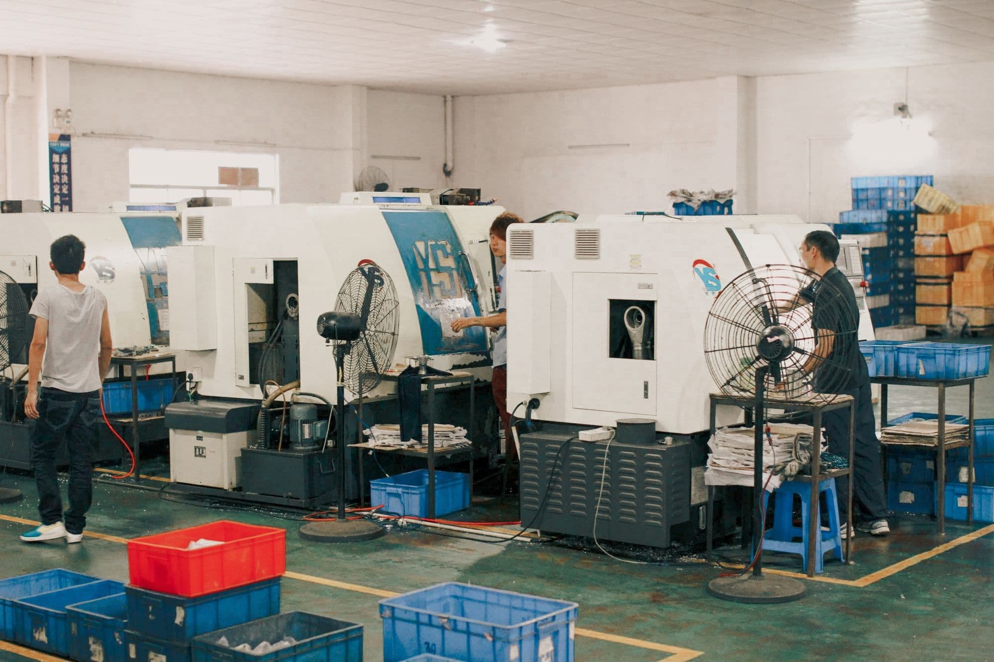 Machinists working at CNC lathes on a supplier shop floor, with parts in crates